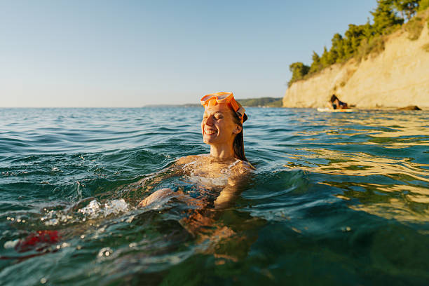 Photo of a young woman swimming in the sea, with a swimming goggles on and a snorkelling equipment